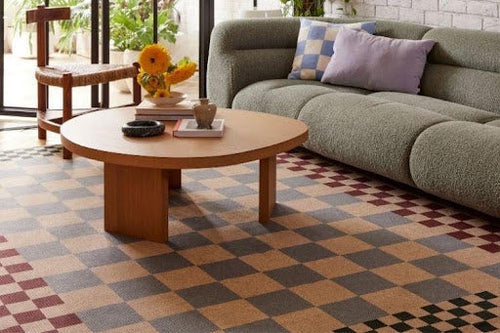 Patterned checkered rug styled under an olive green couch in a sunlit living room with natural warmth.