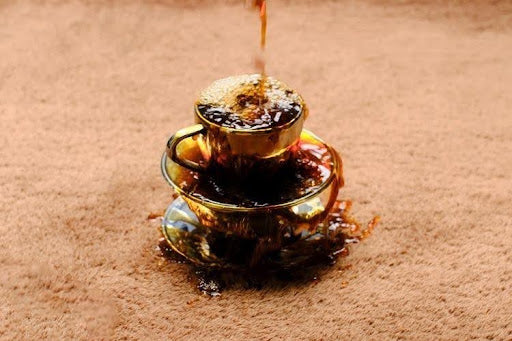 Coffee spilled across a brown wool rug, ready for prompt blotting with a clean cloth.