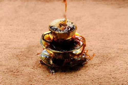 Coffee spilled across a brown wool rug, ready for prompt blotting with a clean cloth.